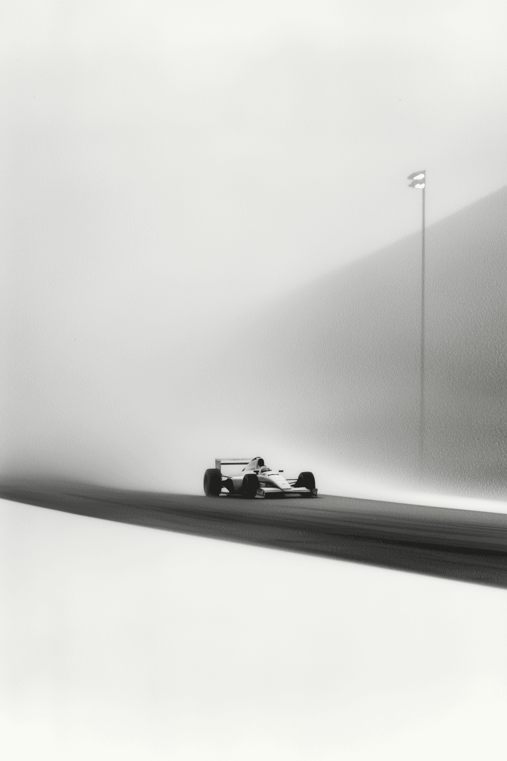 Black and white photograph of a Formula 1 car emerging from thick fog on an open straight